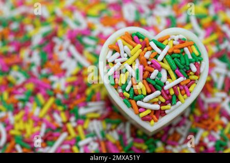 Colorful sugar sprinkles on a heart-shaped cake mold with a colorful background of blurry sugar sprinkles Stock Photo