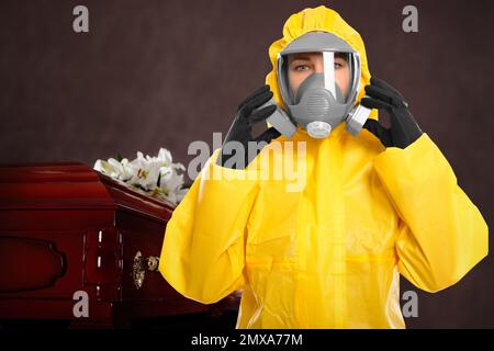 Funeral during coronavirus pandemic. Woman in protective suit near casket indoors Stock Photo
