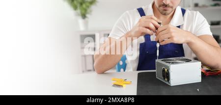 Male technician repairing power supply unit at table indoors, space for text. Banner design Stock Photo