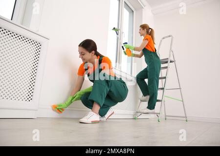 Professional young janitors in uniforms cleaning room Stock Photo