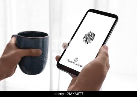 Woman holding smartphone with fingerprint sensor indoors, closeup. Digital identity Stock Photo