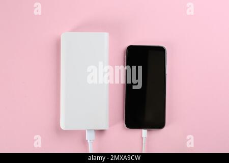 Mobile phone charging with power bank on pink background, flat lay Stock Photo