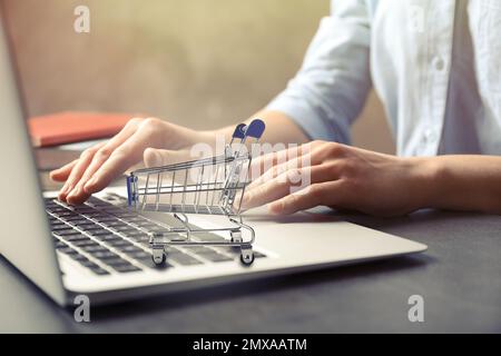 Woman shopping online using laptop, focus on small cart Stock Photo