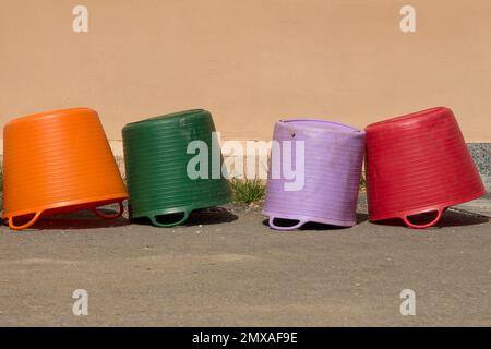 Four colored plastic containers lie upside down near the plastered wall Stock Photo
