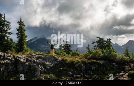 Hiker stretches his arms in the air, in front of cloudy Mt. Shuksan with snow and glacier, dramatic cloudy sky, Mt. Baker-Snoqualmie National Forest Stock Photo