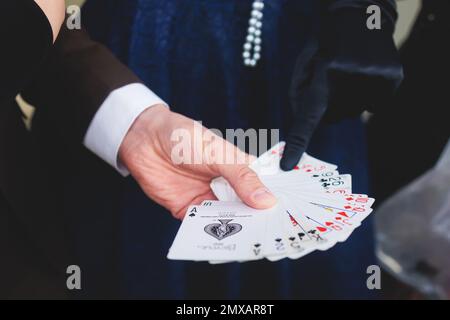 Magician illusionist with a deck of cards showing card tricks focus in front of wealthy rich guests on party event wedding celebration, juggler show, Stock Photo