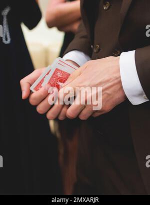 Magician illusionist with a deck of cards showing card tricks focus in front of wealthy rich guests on party event wedding celebration, juggler show, Stock Photo