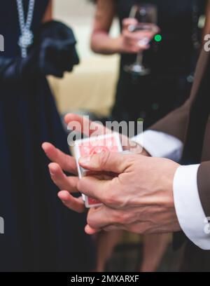 Magician illusionist with a deck of cards showing card tricks focus in front of wealthy rich guests on party event wedding celebration, juggler show, Stock Photo