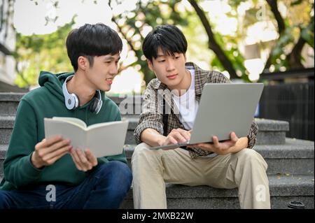 Two young Asian male college students discussing and working on their school project together, using laptop, recheck their final project on laptop tog Stock Photo
