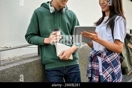 Cropped image of young Asian college students looking at tablet screen, talking and sharing ideas on a school project. Stock Photo