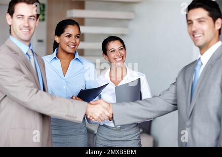 Sealing the deal. Two businessmen sealing the deal with a handshake while their colleagues look on happily. Stock Photo
