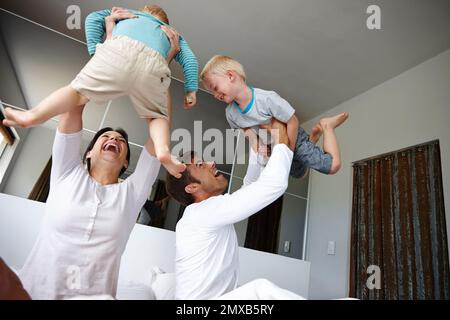 I believe I can fly. two parents playing with their kids at home. Stock Photo