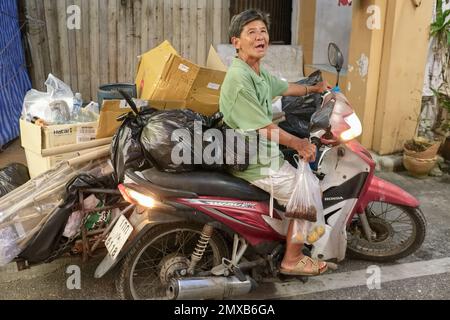 A very cheerful trash collector in Phuket Town, Thailand, a well-known character in town, making the rounds of his motorbike collecting useful trash Stock Photo