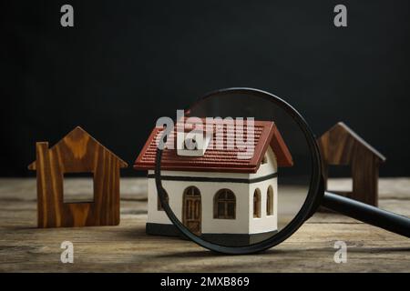 House models and magnifying glass on wooden table. Search concept Stock Photo