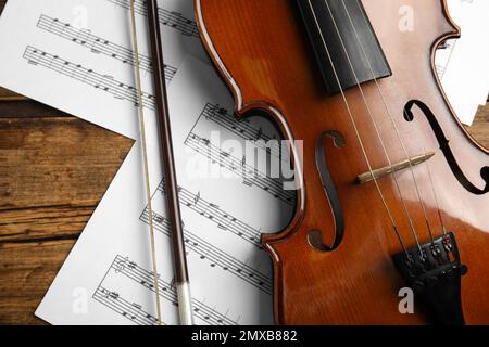 Beautiful violin, bow and note sheets on wooden table, flat lay Stock Photo