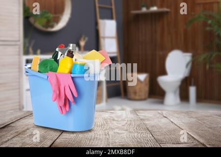 Bucket with cleaning supplies on wooden table in bathroom, space for text Stock Photo