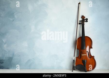Beautiful violin and bow on white wooden table near light blue wall. Space for text Stock Photo