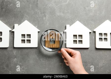 Woman with magnifying glass exploring different house models on grey stone background, top view. Search concept Stock Photo