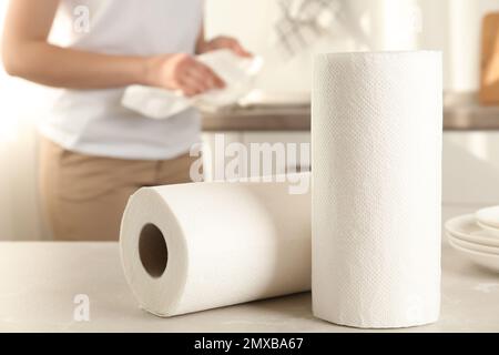 Woman wiping plate with towel in kitchen, focus on paper rolls Stock Photo