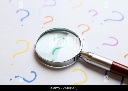 Magnifying glass on sheet of paper with question marks. Search concept Stock Photo