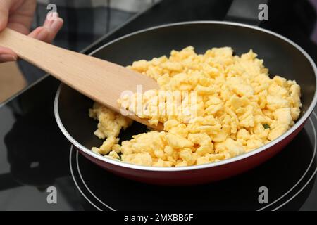 Woman cooking tasty scrambled eggs in frying pan on stove, closeup Stock Photo