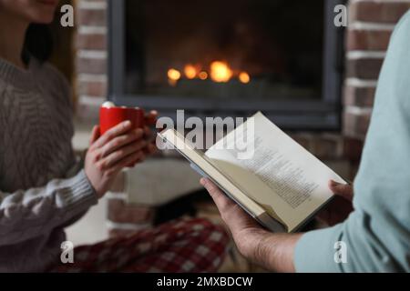 Couple reading book near burning fireplace at home, closeup Stock Photo
