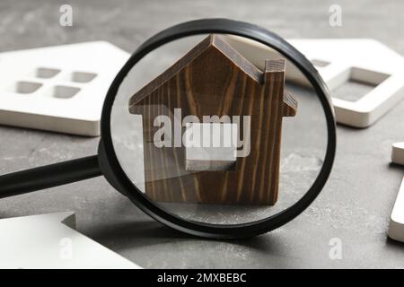 Magnifying glass and house models on grey stone table. Search concept Stock Photo