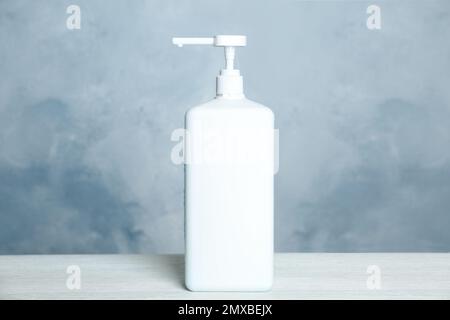 Dispenser bottle with antiseptic gel on table against light background Stock Photo