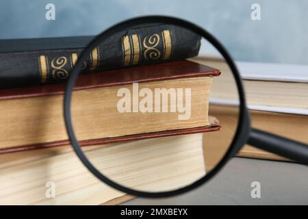 Looking through magnifying glass at stack of vintage books on grey table, closeup. Search concept Stock Photo