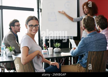 My team is leading the way. Portrait of a young office worker in a meeting with colleagues in the background. Stock Photo