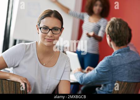Working on this team is a dream. Portrait of a young office worker in a meeting with colleagues in the background. Stock Photo
