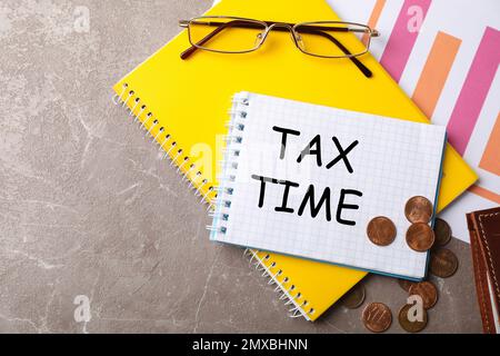 Flat lay composition with stationery, coins, glasses and words TAX TIME written in notebook on table Stock Photo