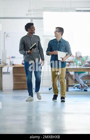 Sharing a laugh at work. a two smiling young coworkers talking together while walking through their office. Stock Photo