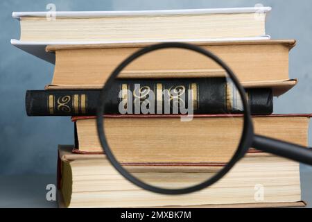 Looking through magnifying glass at stack of vintage books on grey table, closeup. Search concept Stock Photo