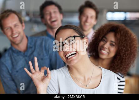 Everything just great. Young woman smiling cheekily at the camera with colleagues in the background. Stock Photo
