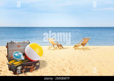 Suitcase with different beach objects on sand near sea Stock Photo