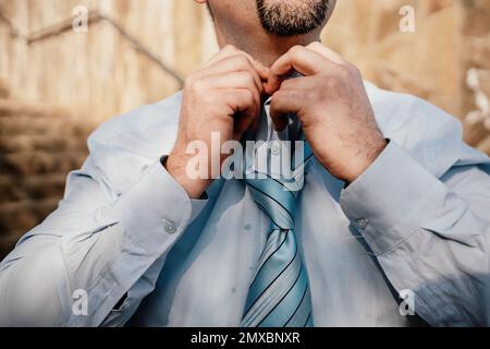 Close up of Man Adjusting Tie of Suit. Businessman in blue shirt straightens his tie, close-up Stock Photo
