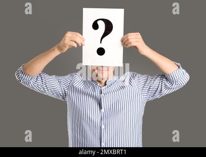 Man holding paper with question mark on grey background Stock Photo