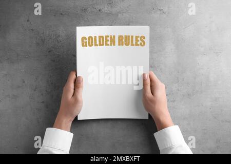 Man holding booklet with phrase GOLDEN RULES at grey table, top view Stock Photo