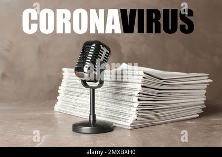 Word CORONAVIRUS, newspapers and vintage microphone on marble table. Journalist's work Stock Photo