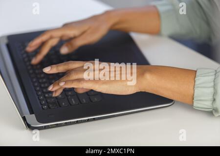 Hands of young adult black woman working on laptop behind white desk in the office. Overhead photo of BIPOC female person typing text on computer Stock Photo