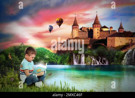 Cute little boy reading magic book near lake and beautiful castle on background Stock Photo
