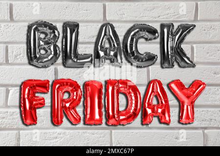 Phrase BLACK FRIDAY made of foil balloon letters against white brick wall Stock Photo