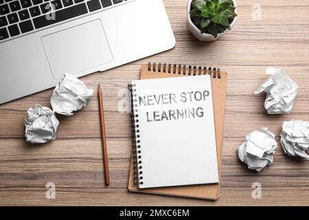 Notebook with phrase NEVER STOP LEARNING and crumpled paper on wooden table, flat lay Stock Photo