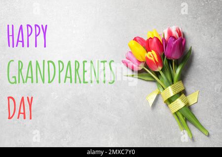 Beautiful spring tulips and phrase HAPPY GRANDPARENTS DAY on light grey stone table, top view Stock Photo