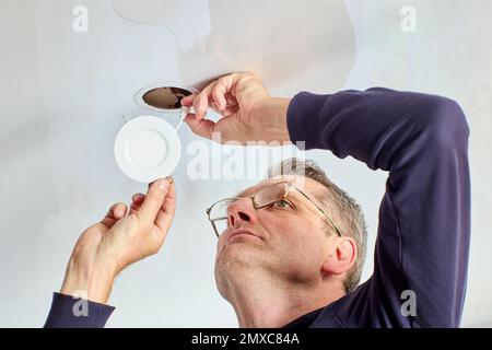 An electrician installs ceiling lighting in living room. Stock Photo