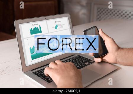 Man working with smartphone and laptop at table indoors, closeup. Forex trading Stock Photo