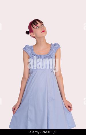 teenager girl in a blue dress dreamily looks up on a light background Stock Photo