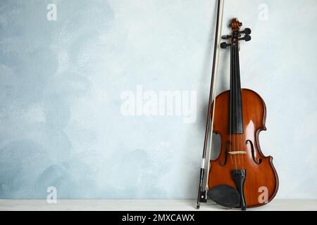 Beautiful violin and bow on white wooden table near light blue wall. Space for text Stock Photo