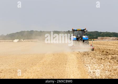 In Parham rural Suffolk a harrowing blue tractor making a drifting dust ...